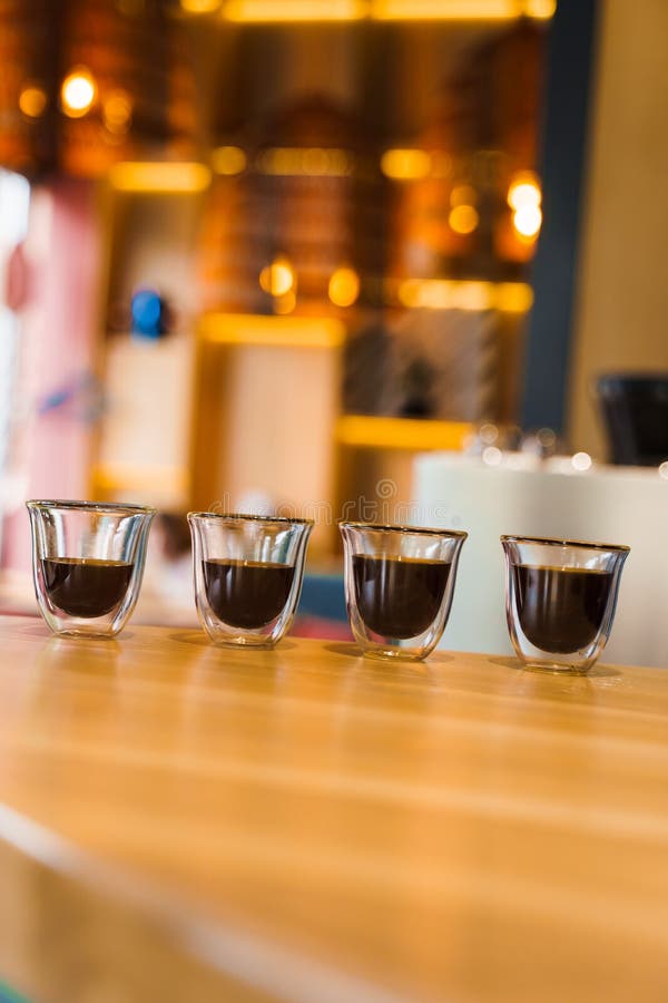 4 Flavored coffee espresso in double glass cup with sun light on background in cafe. Coffee on the wooden table with blurred background. 4 Flavored coffee espresso in double glass cup with sun light on background in cafe. Coffee on the wooden table with blurred background.