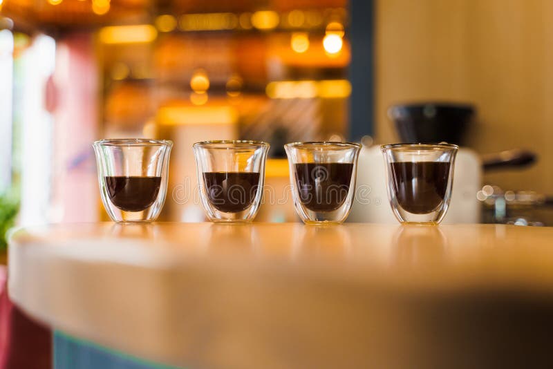 4 Flavored coffee espresso in double glass cup with sun light on background in cafe. Coffee on the wooden table with blurred background. 4 Flavored coffee espresso in double glass cup with sun light on background in cafe. Coffee on the wooden table with blurred background