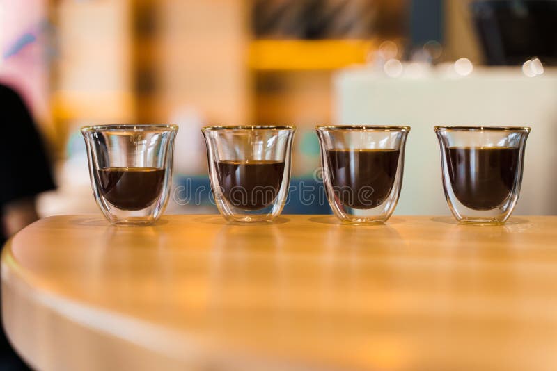 4 Flavored coffee espresso in double glass cup with sun light on background in cafe. Coffee on the wooden table with blurred background. 4 Flavored coffee espresso in double glass cup with sun light on background in cafe. Coffee on the wooden table with blurred background