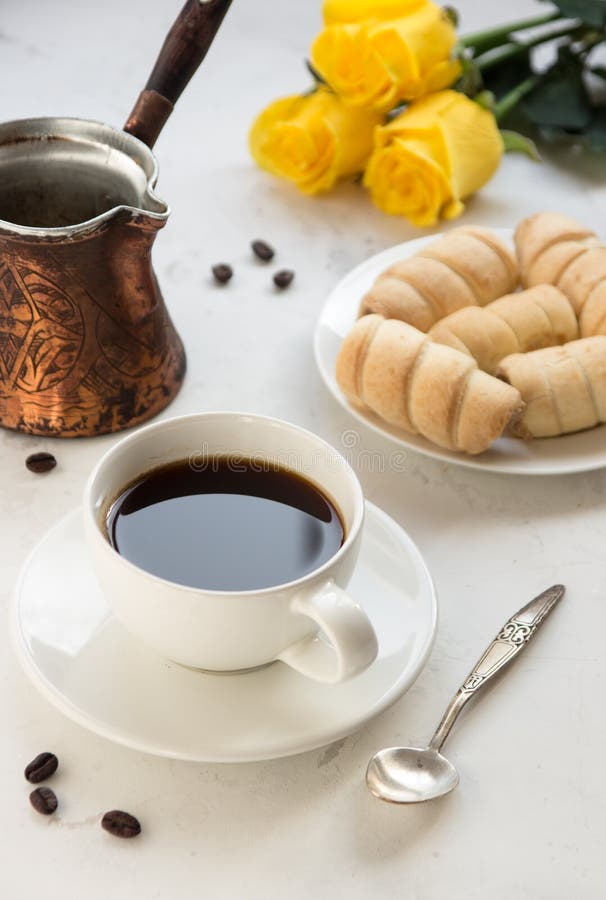 Café, jezva y panadería dulce en una tabla blanca, rosas amarillas encendido imagen de archivo Café, jezva y panadería dulce en una tabla blanca, rosas amarillas encendido imagen de archivo