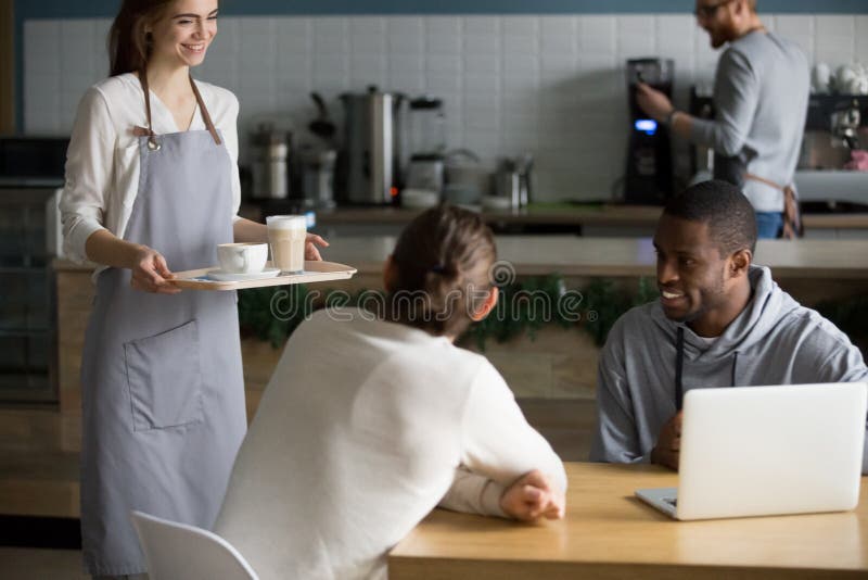 Café joven sonriente del servicio de la camarera a los visitantes masculinos del café imagen de archivo libre de regalías Café joven sonriente del servicio de la camarera a los visitantes masculinos del café imagen de archivo libre de regalías