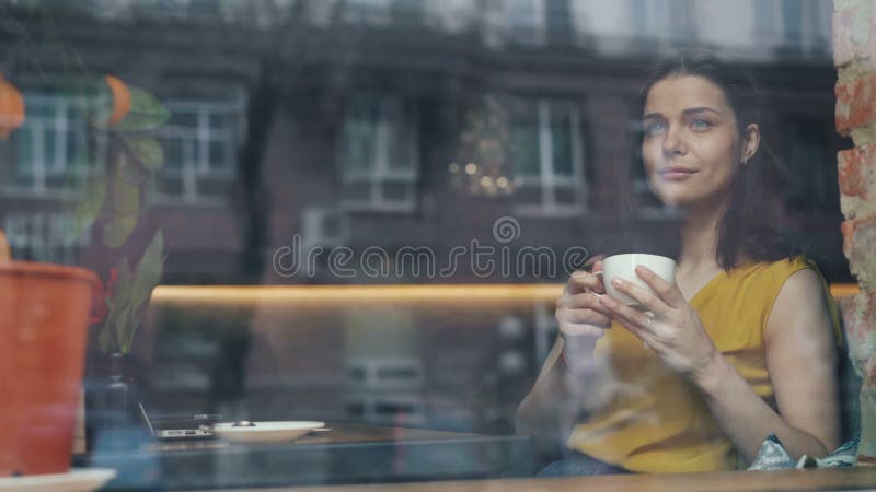 Café potable heureux de jeune dame regardant hors de la fenêtre se reposant en seul café banque de vidéos