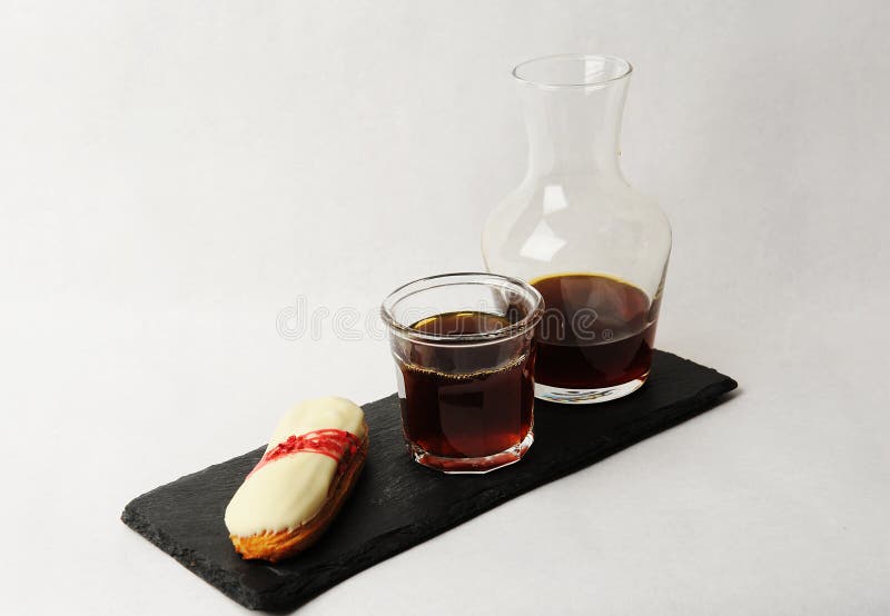 Café recién hecho servido en jarra de vidrio sobre pizarra con eclair. fondo blanco. concepto de especialidad fotografía de archivo