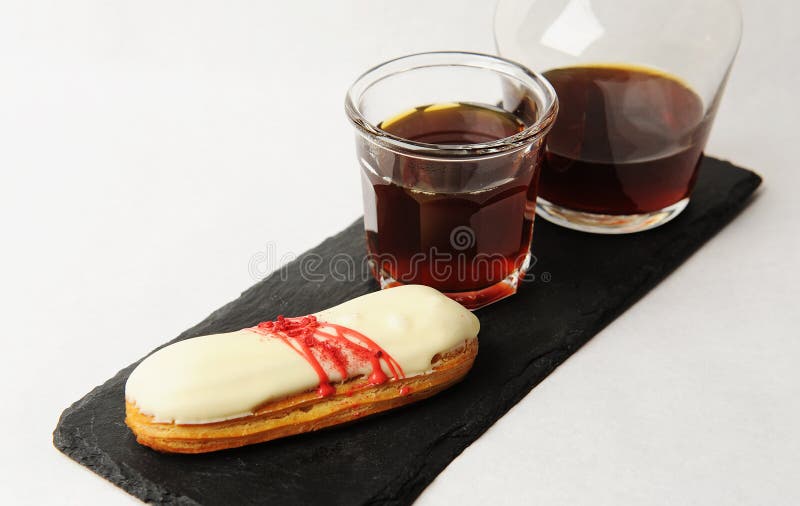 Café recién hecho servido en jarra de vidrio sobre pizarra con eclair. fondo blanco. concepto de especialidad foto de archivo libre de regalías