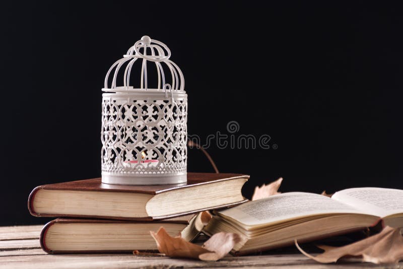 Cage décorative avec la bougie brûlant sur des livres sur le rétro bureau en bois photo libre de droits Cage décorative avec la bougie brûlant sur des livres sur le rétro bureau en bois photo libre de droits