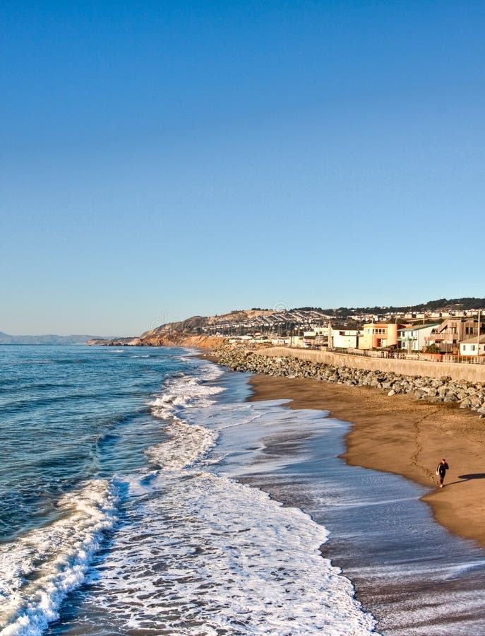 Morning in Pacifica Pier, Pacifica, California, sea. Looking towards the waves, houses, and beach and mountain in distance. A man getting ready to surf in corner. Morning in Pacifica Pier, Pacifica, California, sea. Looking towards the waves, houses, and beach and mountain in distance. A man getting ready to surf in corner