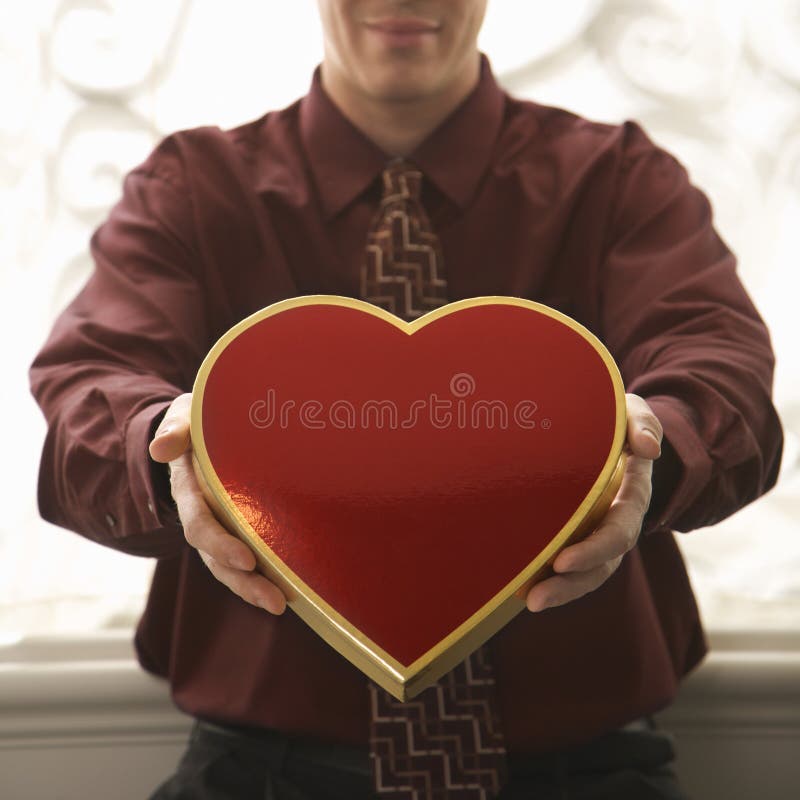 Mid adult Caucasian man holding a heart shaped box of chocolates at viewer. Mid adult Caucasian man holding a heart shaped box of chocolates at viewer.