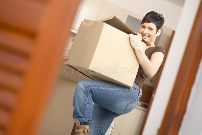 Woman lifting cardboard box while moving home, smiling. Woman lifting cardboard box while moving home, smiling.