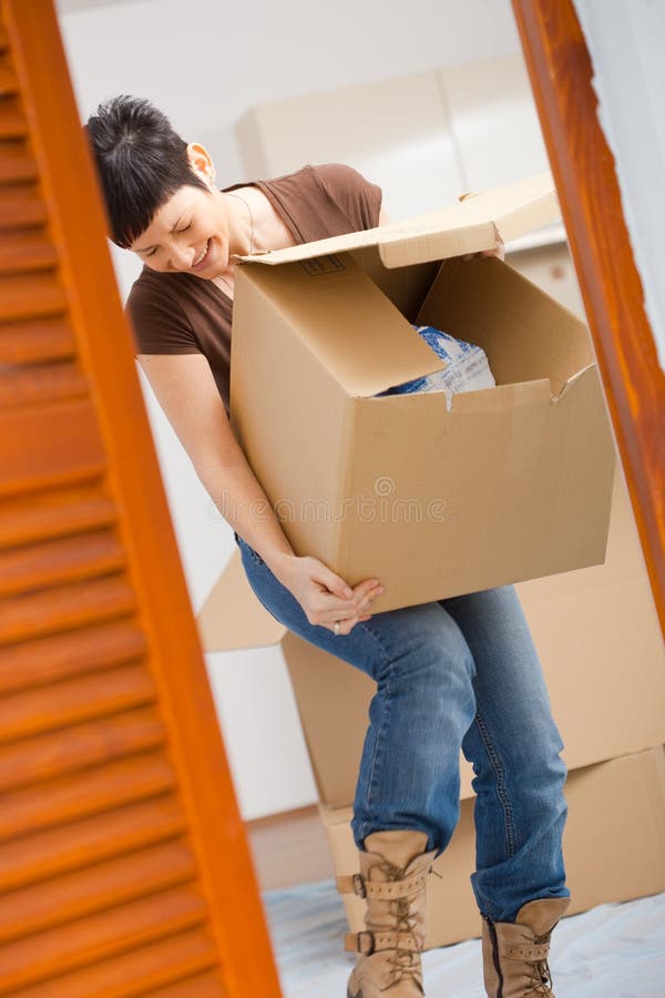 Woman lifting cardboard box while moving home, smiling. Woman lifting cardboard box while moving home, smiling.