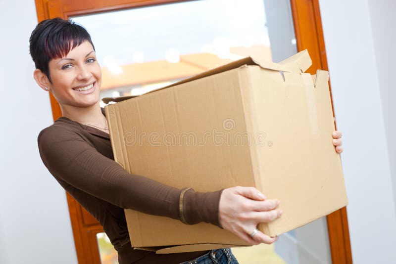 Woman lifting cardboard box while moving home, smiling. Woman lifting cardboard box while moving home, smiling.