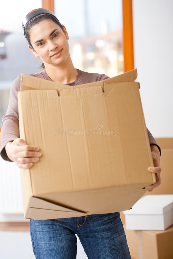 Woman lifting cardboard box while moving home, smiling. Woman lifting cardboard box while moving home, smiling.