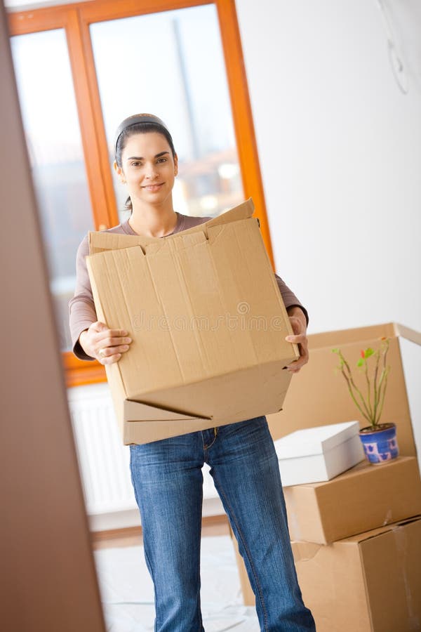 Woman lifting cardboard box while moving home, smiling. Woman lifting cardboard box while moving home, smiling.