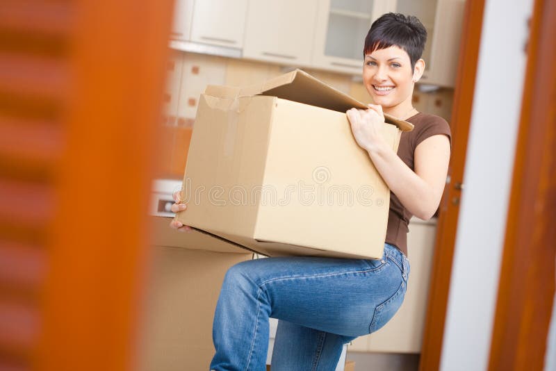 Woman lifting cardboard box while moving home, smiling. Woman lifting cardboard box while moving home, smiling.