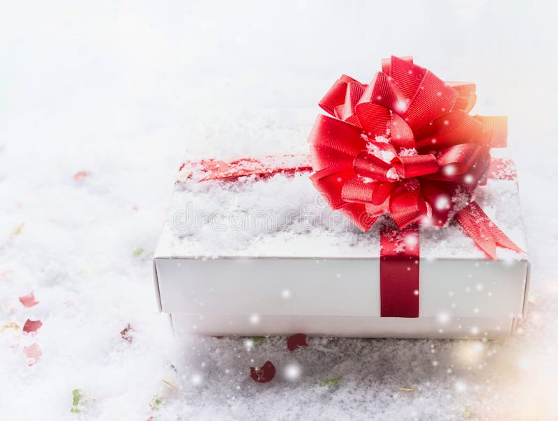 Caixa de presente branca com curva vermelha na neve com bokeh e queda de neve copie o espaço para seu projeto imagens de stock Caixa de presente branca com curva vermelha na neve com bokeh e queda de neve copie o espaço para seu projeto imagens de stock