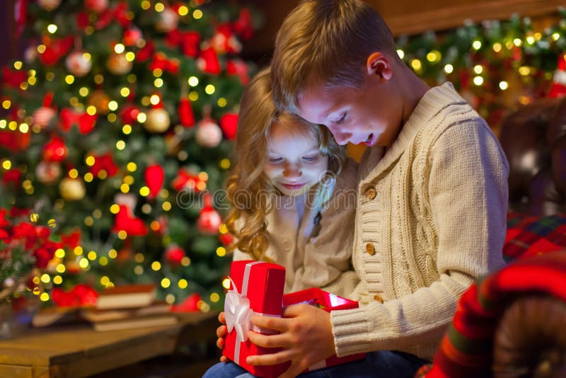 Caixa de presente mágica do Natal crianças no sofá em uma obscuridade acolhedor imagem de stock Caixa de presente mágica do Natal crianças no sofá em uma obscuridade acolhedor imagem de stock