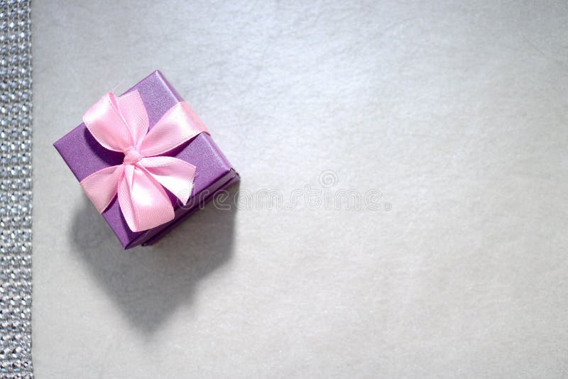 Caixa de presente pequena com uma curva em uma luz - fundo cinzento do cartão festivo bonito violeta do presente imagem de stock royalty free Caixa de presente pequena com uma curva em uma luz - fundo cinzento do cartão festivo bonito violeta do presente imagem de stock royalty free
