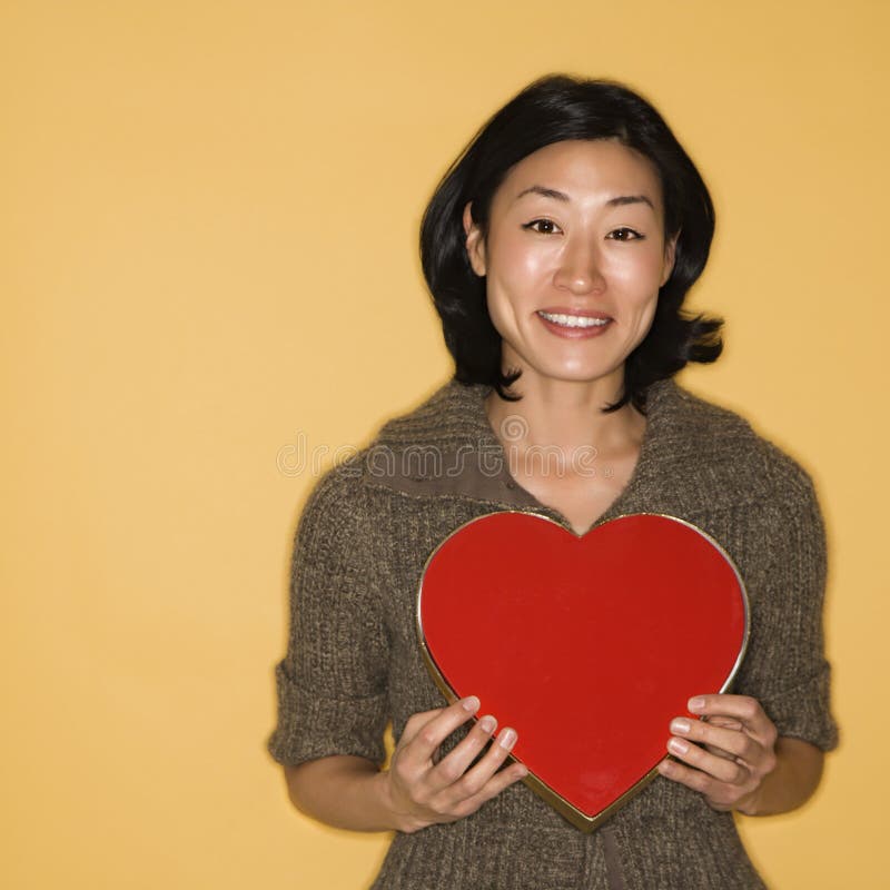 Pretty mid adult Asian woman holding red heart shaped box. Pretty mid adult Asian woman holding red heart shaped box.