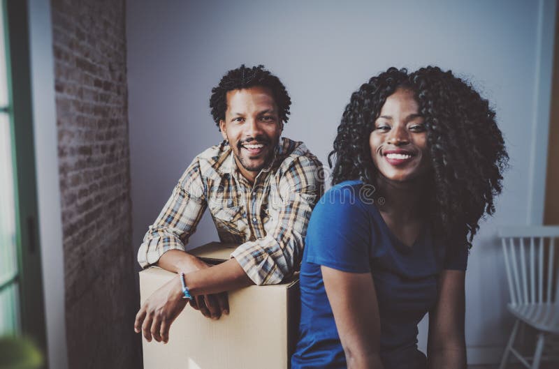 Caixas moventes dos pares novos felizes do africano negro no apartamento novo junto e fazendo uma vida bem sucedida Família alegr imagem de stock royalty free Caixas moventes dos pares novos felizes do africano negro no apartamento novo junto e fazendo uma vida bem sucedida Família alegr imagem de stock royalty free