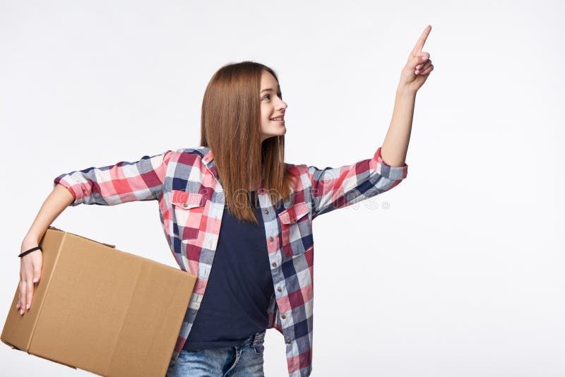 Delivery, relocation and unpacking. Smiling young woman holding cardboard box and pointing finger up or pushing imaginary button. Delivery, relocation and unpacking. Smiling young woman holding cardboard box and pointing finger up or pushing imaginary button