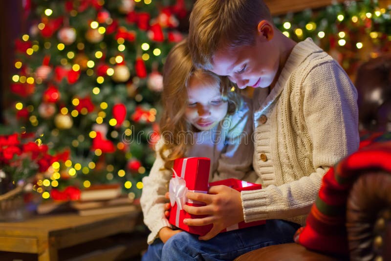 Caja de regalo mágica de la Navidad niños en el sofá en una oscuridad acogedora imagenes de archivo Caja de regalo mágica de la Navidad niños en el sofá en una oscuridad acogedora imagenes de archivo