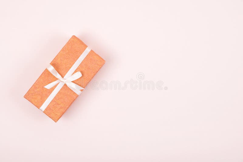 Caja de regalo simple adornada con la cinta blanca del arco en fondo rosado en colores pastel Endecha plana fotografía de archivo libre de regalías Caja de regalo simple adornada con la cinta blanca del arco en fondo rosado en colores pastel Endecha plana fotografía de archivo libre de regalías