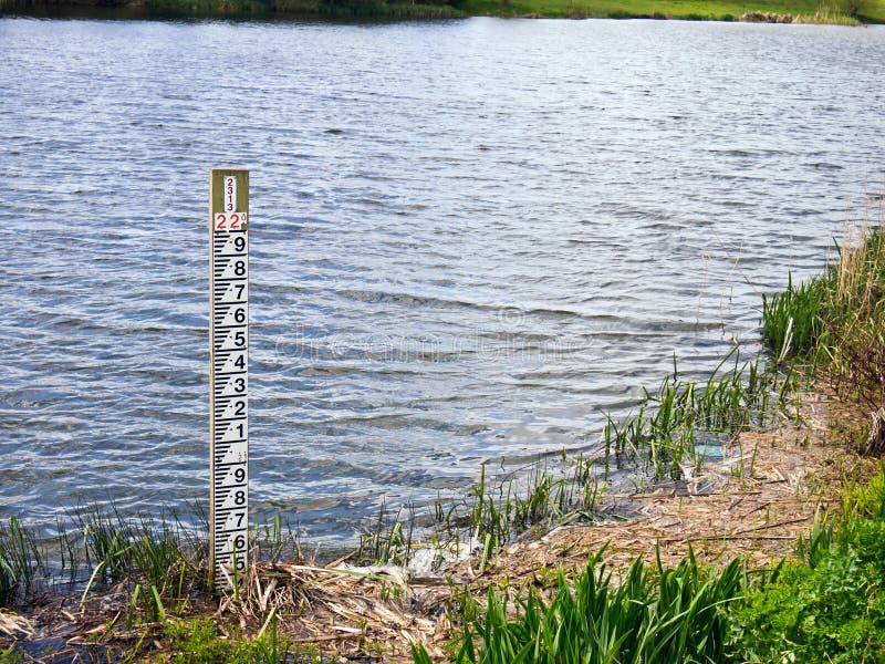 Vertical water level gauge pole near the bank of a wide river. Jubilee River, near Taplow, Buckinghamshire, England. Vertical water level gauge pole near the bank of a wide river. Jubilee River, near Taplow, Buckinghamshire, England.