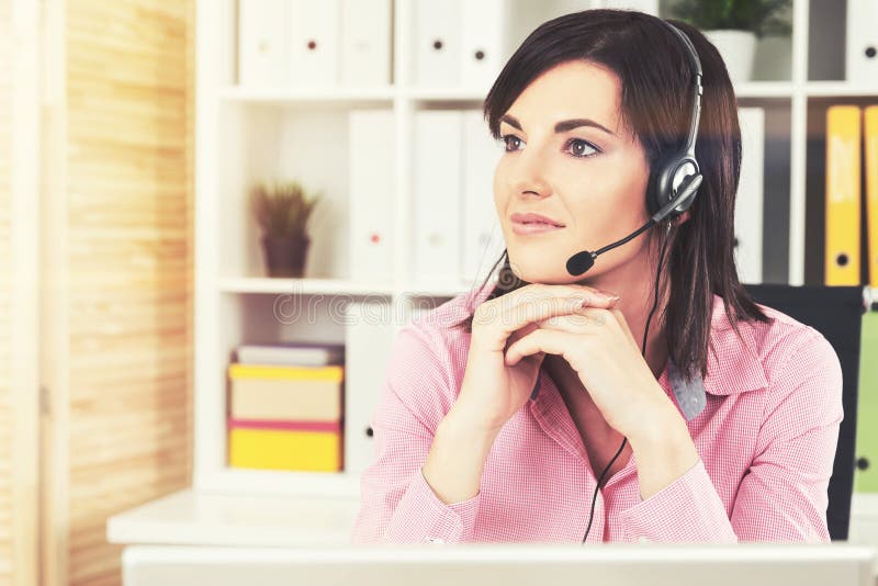 Portrait of a pensive young call center employee with a headset at her workplace in a modern office. Toned image. Portrait of a pensive young call center employee with a headset at her workplace in a modern office. Toned image