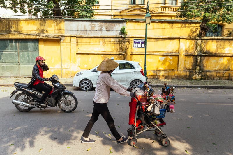 Calle de Hanoi con un hombre que conduce la motocicleta y a la mujer con el carro al por menor móvil y el coche móvil en Vietnam imagen de archivo libre de regalías Calle de Hanoi con un hombre que conduce la motocicleta y a la mujer con el carro al por menor móvil y el coche móvil en Vietnam imagen de archivo libre de regalías