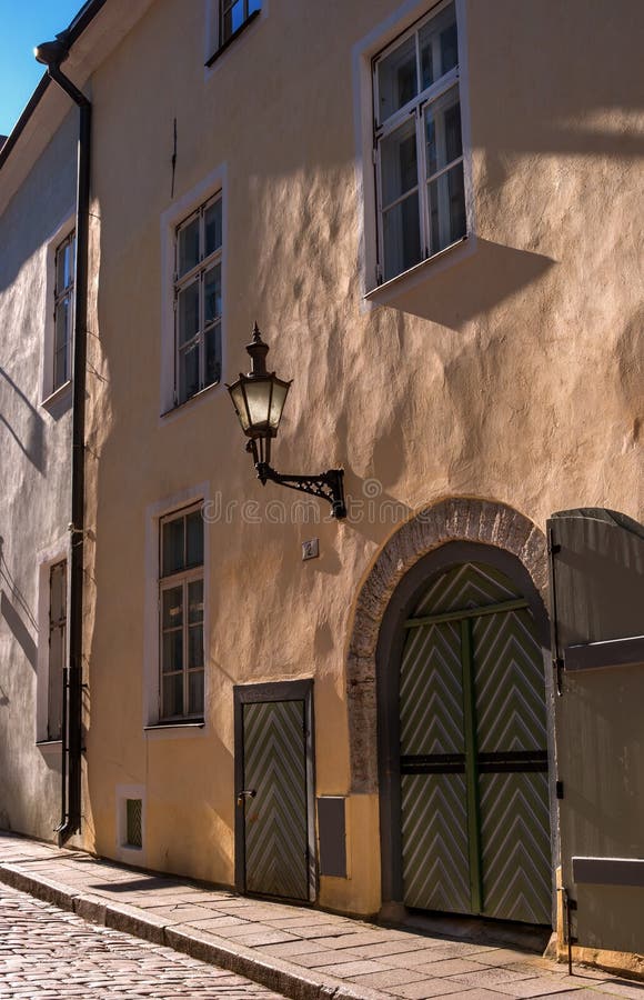 Traditional street of old Tallinn, Estonia. Old wall street lamp. Wooden gate and old wooden door. The walls of the houses are plastered. The street is paved with cobblestones. Traditional street of old Tallinn, Estonia. Old wall street lamp. Wooden gate and old wooden door. The walls of the houses are plastered. The street is paved with cobblestones.