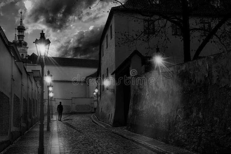 Callejón estrecho evocador de Praga en la oscuridad, con las luces de calle encendido y la silueta de un hombre que camina en los