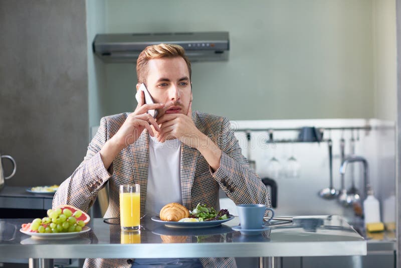 Pensive man speaking on smartphone by dinner table during breakfast at home. Pensive man speaking on smartphone by dinner table during breakfast at home