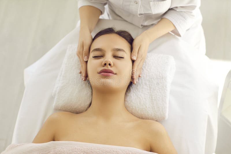 Calm Beautiful Woman Enjoys Relaxing Facial Massage Given To Her By Specialist In Spa Stock