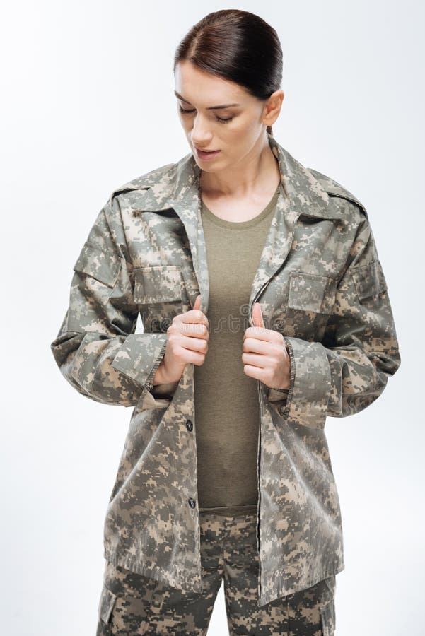 Tranquil beautiful female soldier putting on combat jacket and staying righ...