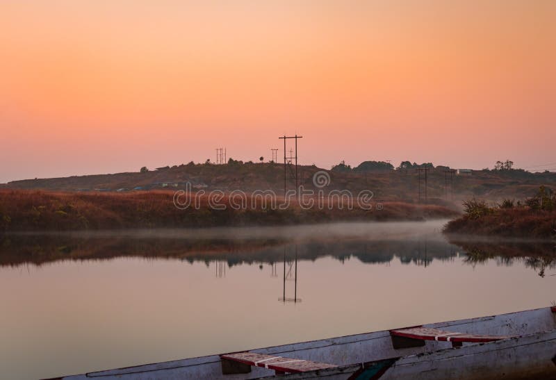 Calm lake with white mists and dramatic sunrise orange sky reflection at morning in details.