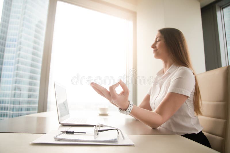 Calm peaceful businesswoman practicing yoga at work, meditating