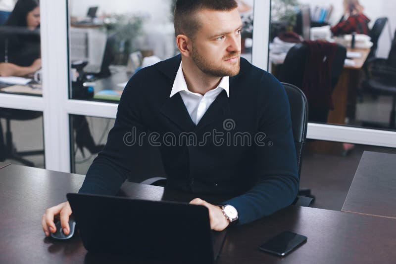 Calm serious young man uses laptop to work at table in office stock photo Calm serious young man uses laptop to work at table in office stock photo