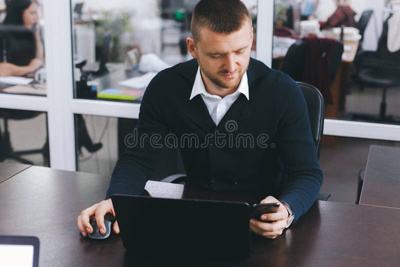 Calm serious young man uses phone while working at table in office royalty free stock photos Calm serious young man uses phone while working at table in office royalty free stock photos