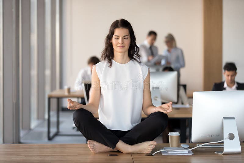 Calm young businesswoman doing yoga exercise at work desk