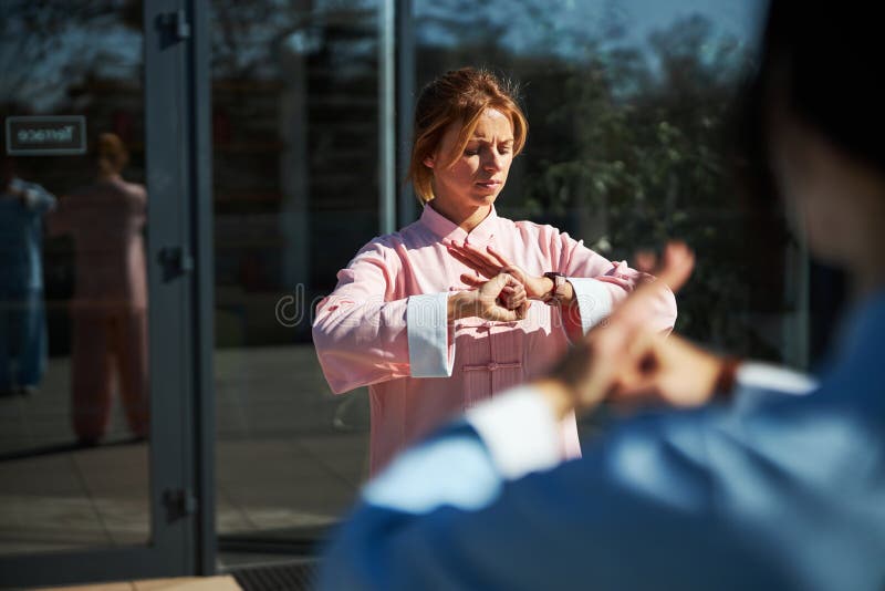 Calm young women in a pink Chinese suit standing outdoors with closed eyes and putting hands together. Qigong class stock images, royalty-free photos and pictures