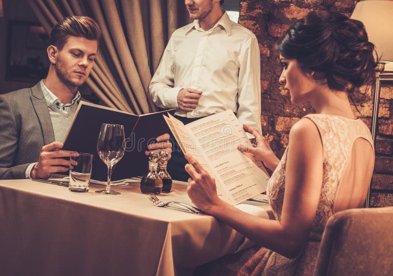 Camarero que explica el menú a los pares ricos en restaurante foto de archivo Camarero que explica el menú a los pares ricos en restaurante foto de archivo