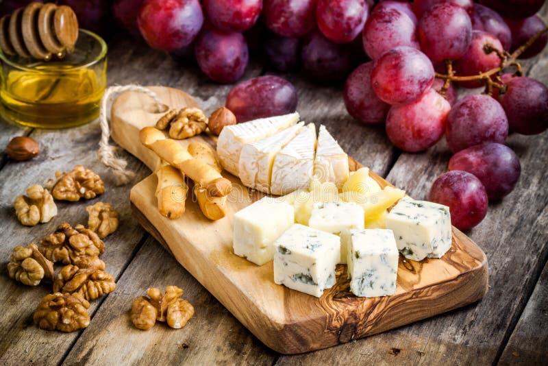 Camembert, parmesano, queso verde con las barras de pan, nueces, miel y uvas foto de archivo libre de regalías Camembert, parmesano, queso verde con las barras de pan, nueces, miel y uvas foto de archivo libre de regalías