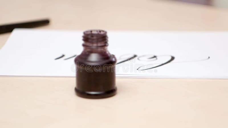 Camera moves along the desk with calligraphic tools. Close shot. Side view. Inkpot with black paint. Brush pen and blank