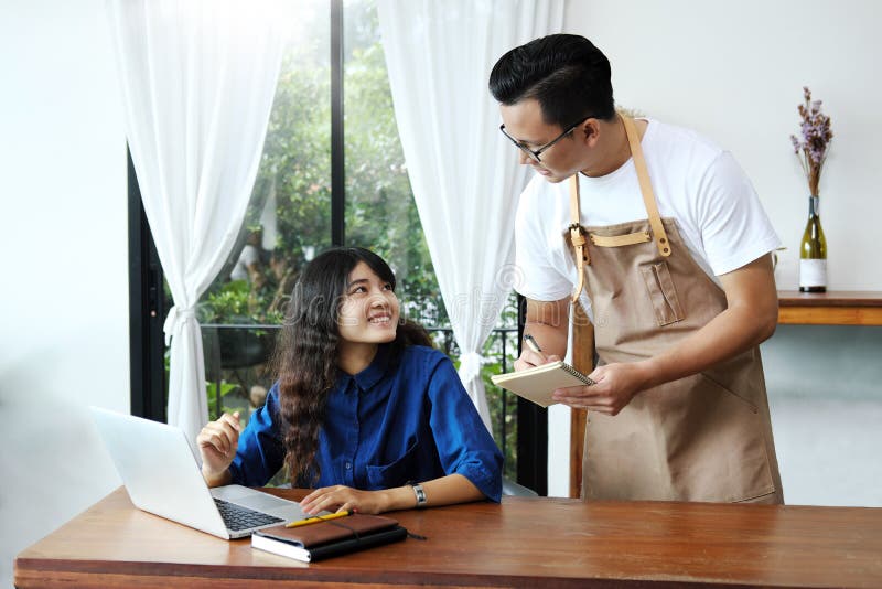 Cameriera di bar asiatica dell'uomo che prende ordine della donna nel caffè Resta del caffè fotografie stock libere da diritti Cameriera di bar asiatica dell'uomo che prende ordine della donna nel caffè Resta del caffè fotografie stock libere da diritti
