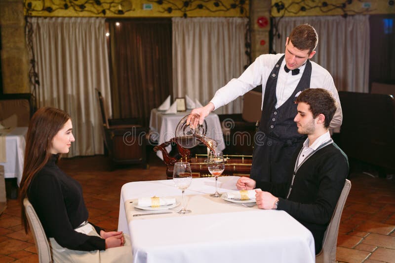 Cameriere che versa vino rosso in un vetro ad una tavola del ristorante fotografia stock Cameriere che versa vino rosso in un vetro ad una tavola del ristorante fotografia stock