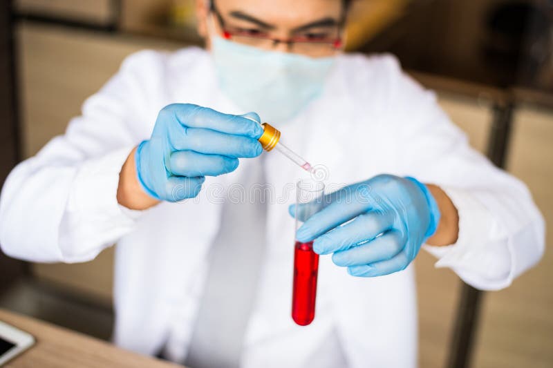 Camice di usura dello scienziato e guanti blu che reggono contagoccia e rosso di goccia alla scienza del tubo Il chimico esamina fotografia stock Camice di usura dello scienziato e guanti blu che reggono contagoccia e rosso di goccia alla scienza del tubo Il chimico esamina fotografia stock