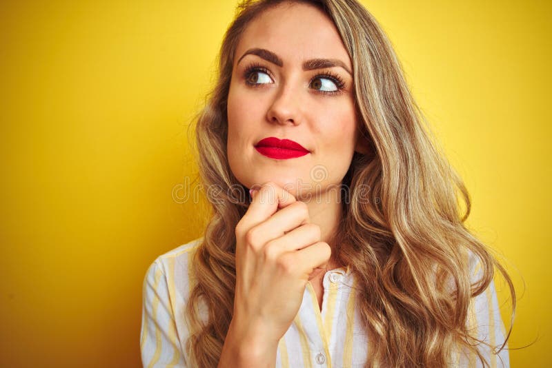 Camicia d'uso delle bande della giovane bella donna che controlla la faccia seria isolato giallo del fondo che pensa alla domanda fotografia stock libera da diritti