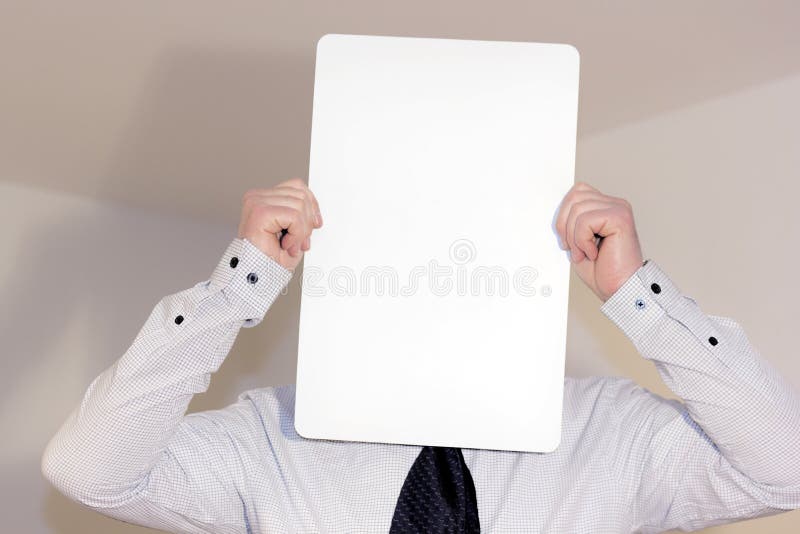 Camicia d'uso e legame del giovane che tengono bord verticale bianco davanti al suo fronte immagine stock libera da diritti Camicia d'uso e legame del giovane che tengono bord verticale bianco davanti al suo fronte immagine stock libera da diritti