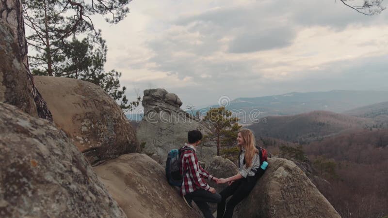 Caminantes románticos que se sientan en el top de la montaña, charlando, y disfrutando de su tiempo junto Un muchacho con una sup