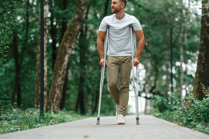 Caminar por el hermoso parque. el hombre con muletas está afuera. lesión en la pierna fotografía de archivo libre de regalías