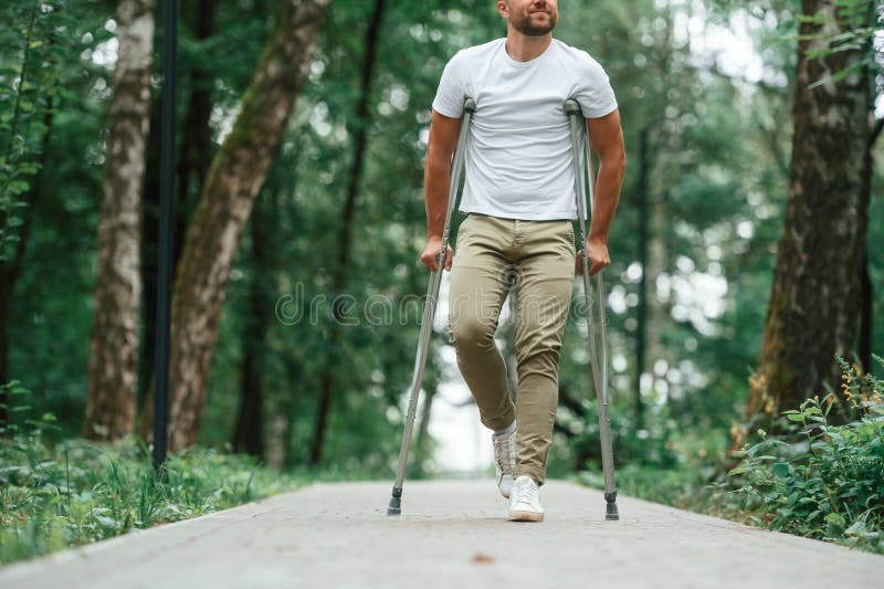 Caminar por el hermoso parque. el hombre con muletas está afuera. lesión en la pierna foto de archivo libre de regalías
